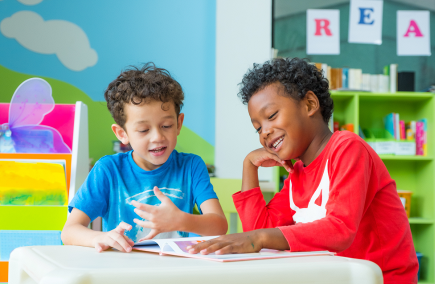 Imagination Bus Image: Two young boys laugh and enjoy a book whilst sitting at a table. 