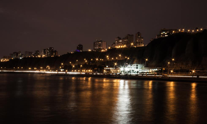 Lima Nightlife Image: View of the city from the coastline, lit up at night.