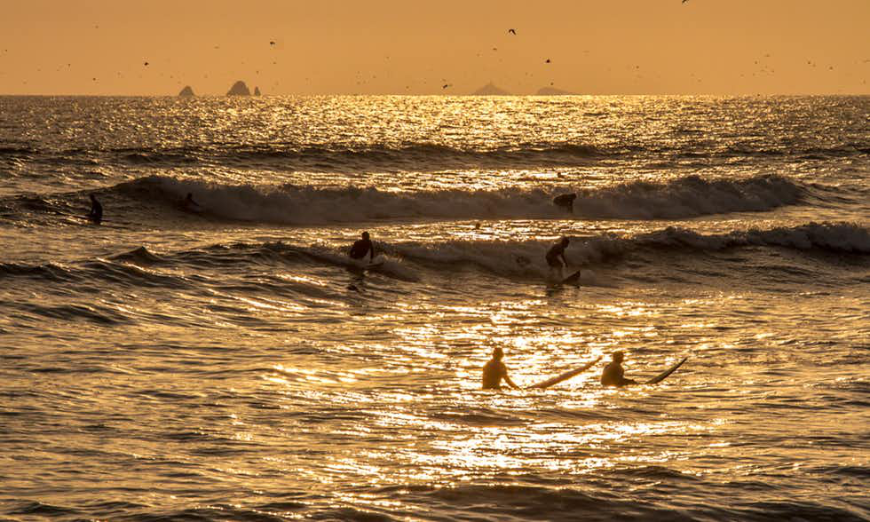 Lima Nightlife Image: Surfers come in from waves as the sun sets on the ocean.