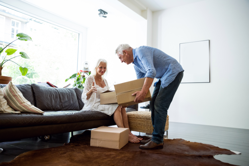 Moving Abroad Image: A mature silver haired couple unpacks boxes in their home.