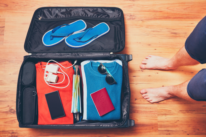 Moving to Belize Image: A man's stands over his suitcase; we see his shorts and feet. The suitcase has colorful casual clothing, an electronic charger, sunglasses, passport, and flip-flops.