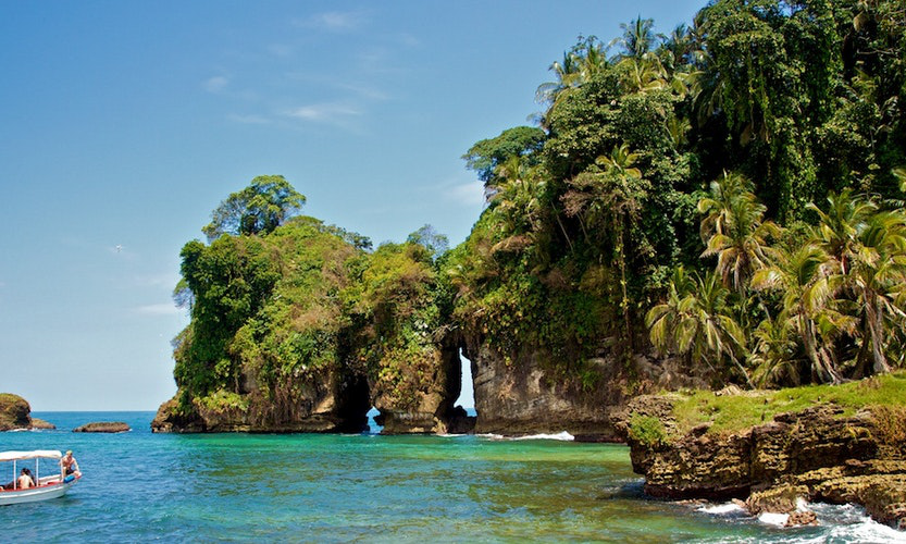 Moving to Panama Image: Formations covered in lush green foliage in the midst of a clear green sea.