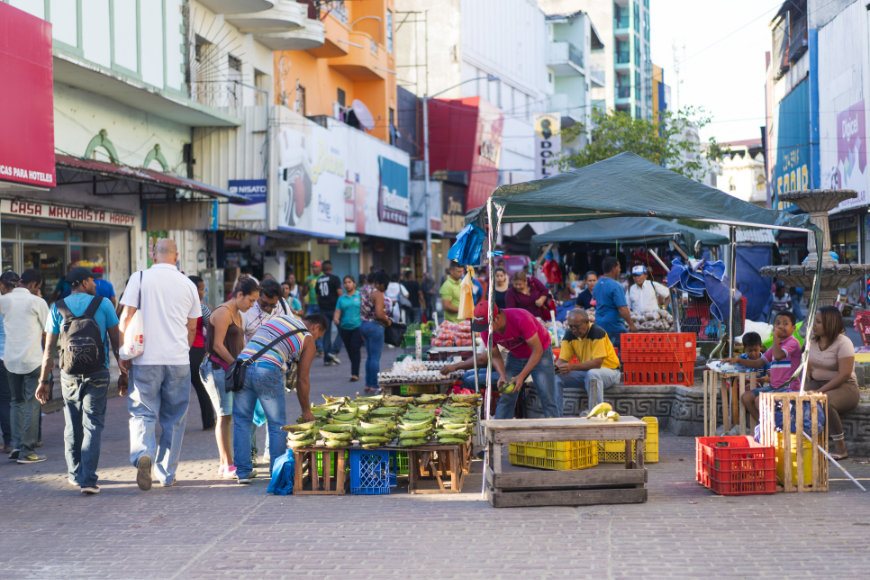 Moving to Panama Image: An outdoor market is full of stalls; people mill about what appears to be a fruit stand.