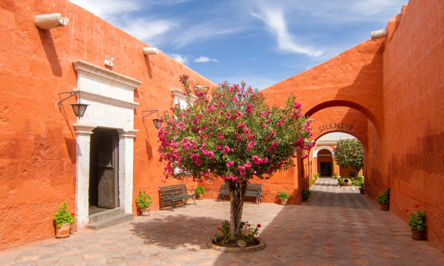 Peru Group Tour Image: An orange building and archway at the monastery; pink flowers are on a tree.
