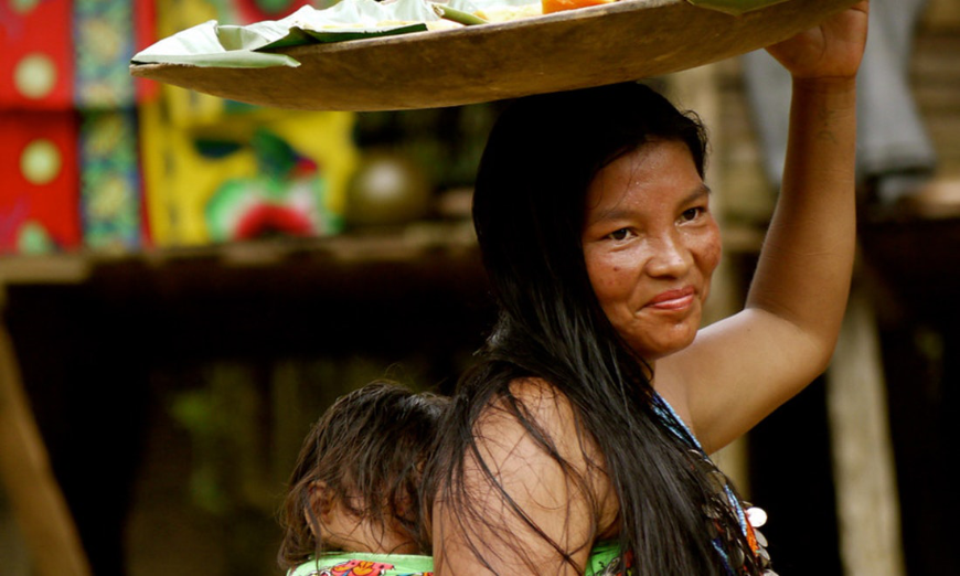 Summer In Panama Image: A female member of the Emberà smiles whilst carrying a baby on her back and holding a platter on her head.