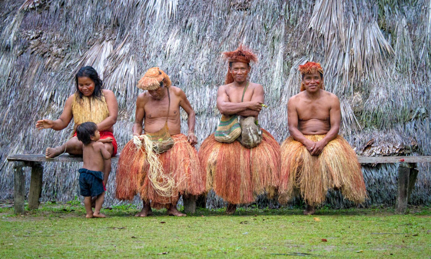 Sustainable Travel In Peru Image: One female member and child, and three male members of the Yagua Tribe sit on a bench.