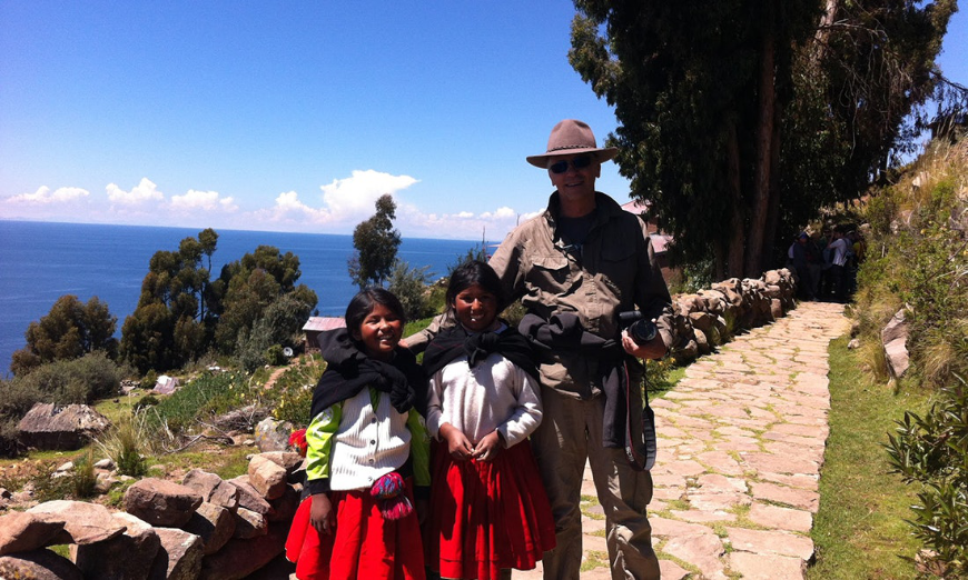 Sustainable Travel In Peru Image: A man in khakis poses with two young Peruvian women wearing red skirts, white blouses, and black wraps. 