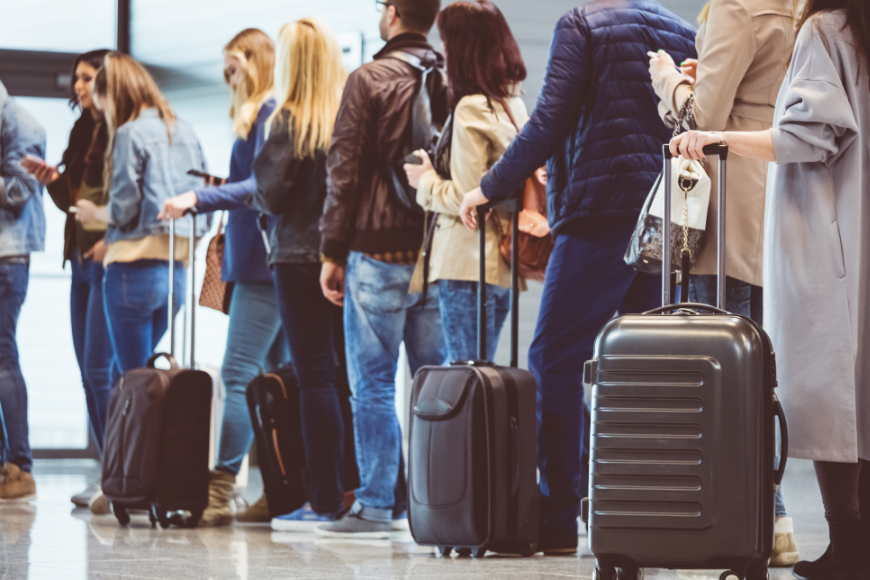 Sustainable Travel Image: A line of travelers is queued in an airport with their luggage.