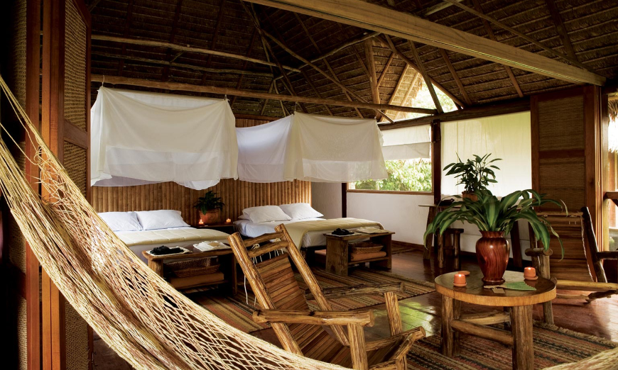 Sustainable Travel Practices Image: Interior view of an ecolodge room complete with canopy beds, hammock, plants, and wooden furniture. 