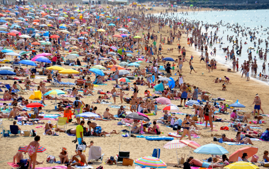 Tropical Holiday Image: A crowded beach full of other tropical holiday revelers with their sun umbrellas, beach towels, and toys all over the beach and in the water.