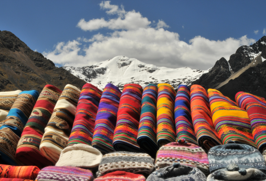 Peru Souvenir Image: Colorful, traditional fabrics displayed on a stall on La Raya pass in the heart of the Inca land, Andes, Peru. Snow and glacier covered peak of Chimbuya (5600 m) visible in the background.