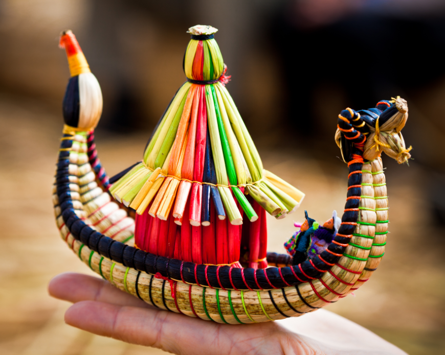 Peru Souvenir Image: A person (not shown) holds a small colourful reed boat—a Peruvian souvenir from Uros island—in the palm of their hand.