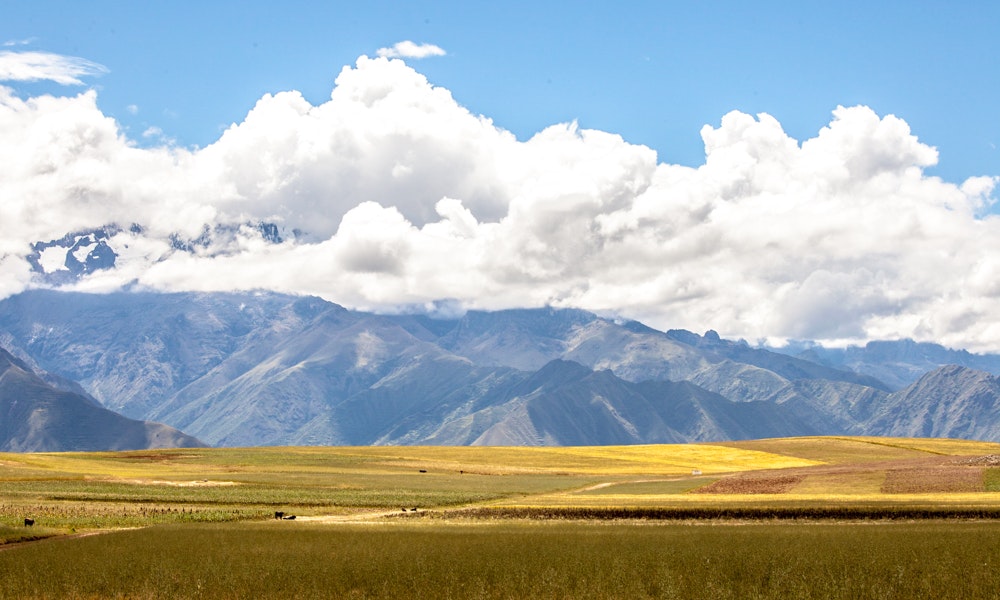 Unique Peru Image: An image of the Sacred Valley shows fields of green and gold, a mountain, and a flurry of clouds dividing the mountain from the azure sky.