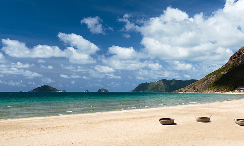 Vietnam Island Destinations Image: Water gently laps a beach, while blue skies and puffy white clouds grace the sky in the background.