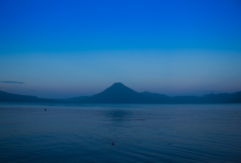 What To Pack Image: A lovely early-morning photograph of Guatemala's Lake Atitlán. The sky is painted in shades of dusty rose and hues of blue; gentle ripples are formed across the water.