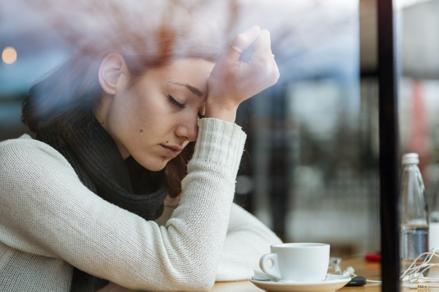 Why Travel Insurance Is A Must Image: A woman sits in a cafe with her head in her hand, obviously stressed.