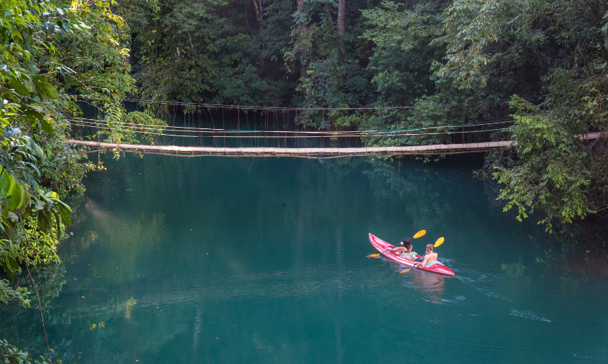 Why Travel Insurance Is A Must Image: Two people enjoy kayaking on vibrant water, surrounded by forest.